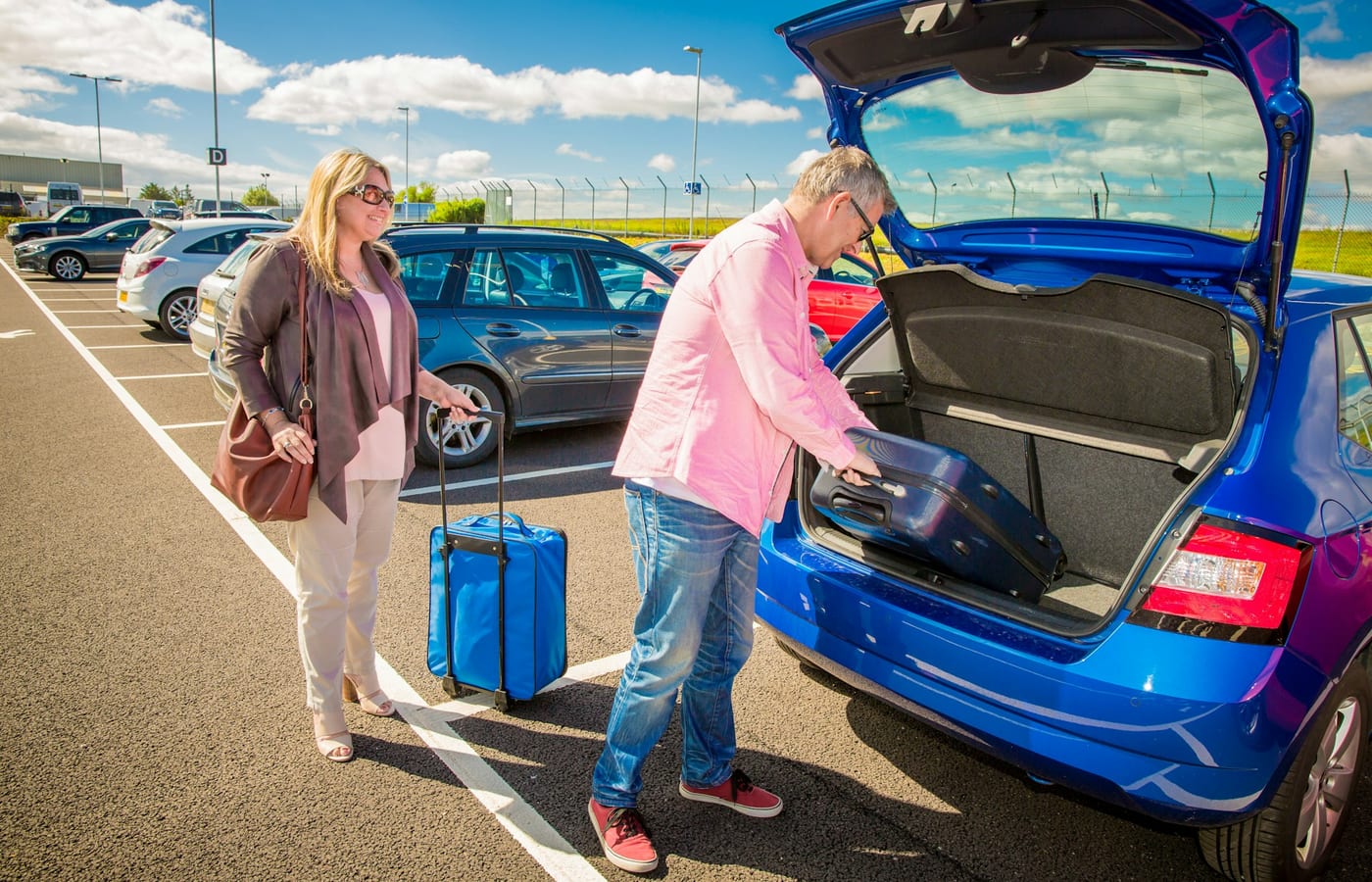 Two people loading suitcases into the boot of a car in a car park