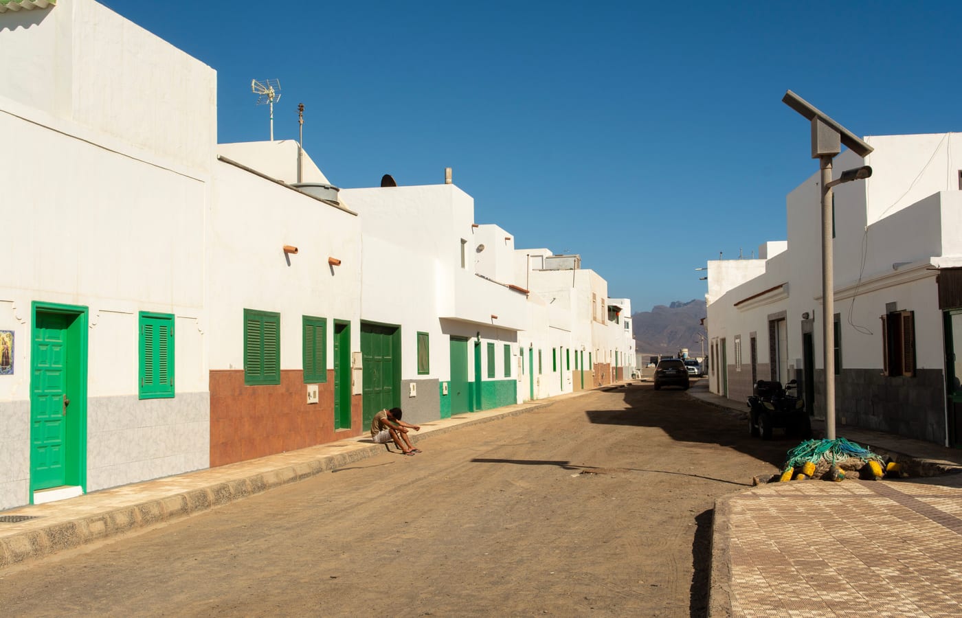 A quiet white-walled street in El Médano with green shutters and a bicycle