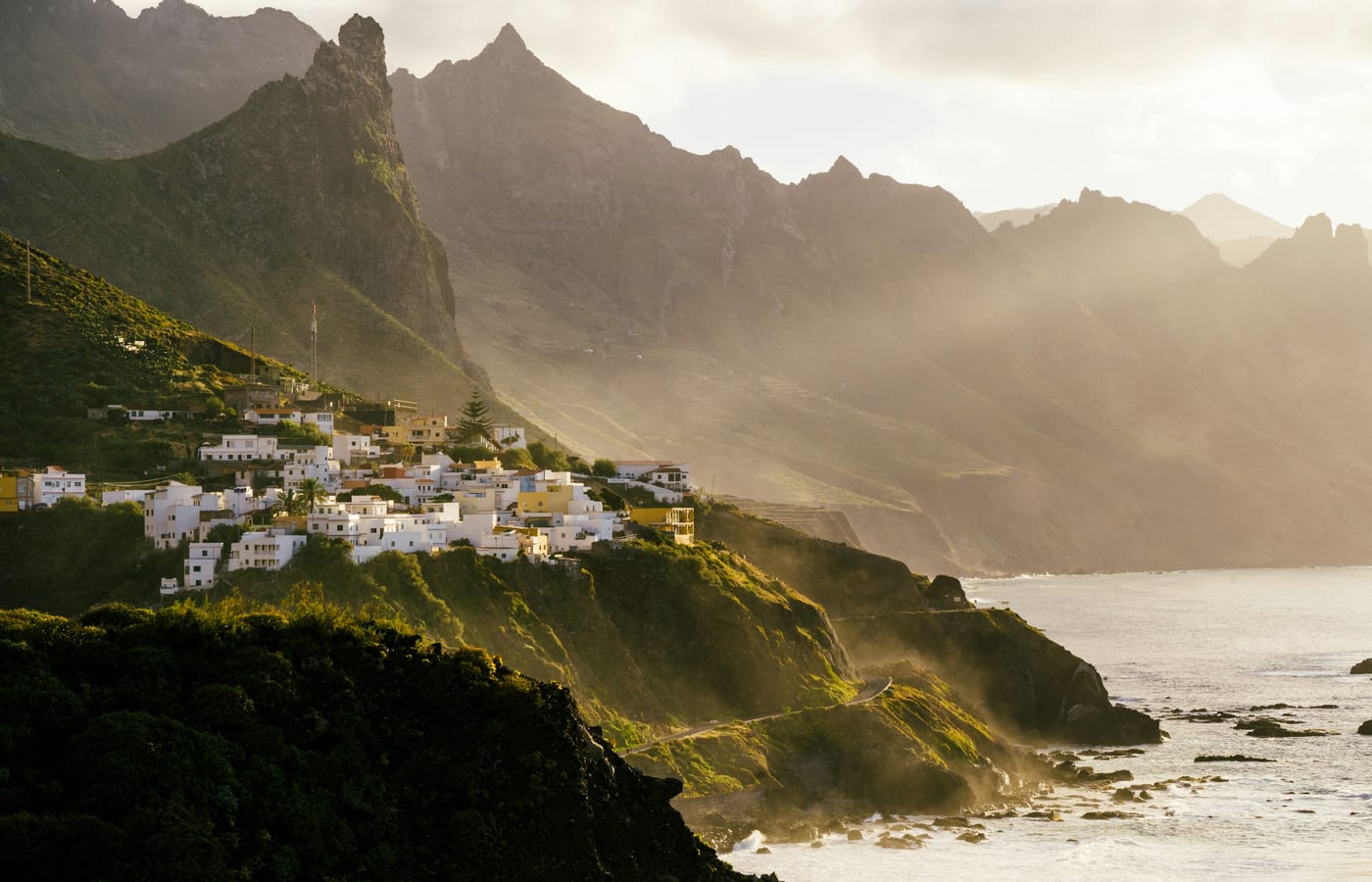 A village on a ridge in the Anaga hills with sunlight breaking through cloud over the sea