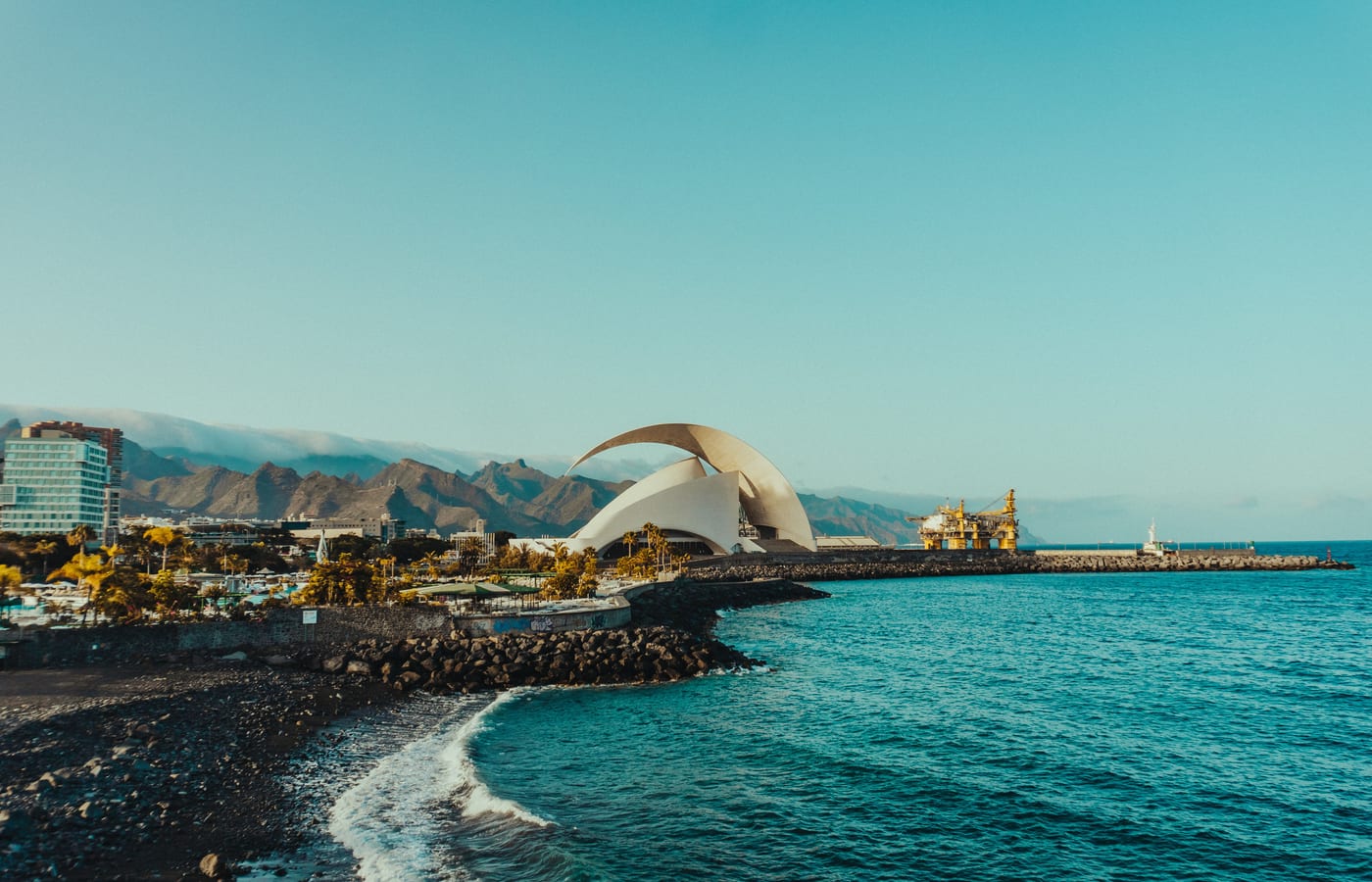 The curved white auditorium of Santa Cruz beside turquoise water and the harbour wall