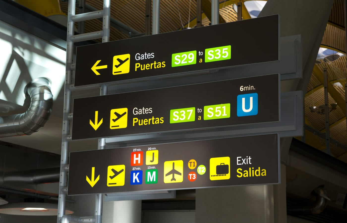 Yellow overhead signage in a Spanish airport terminal pointing to the gates and the exit
